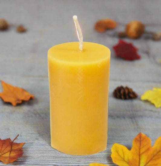 Yellow candle with a wick on a wooden surface with autumn leaves and pinecones.