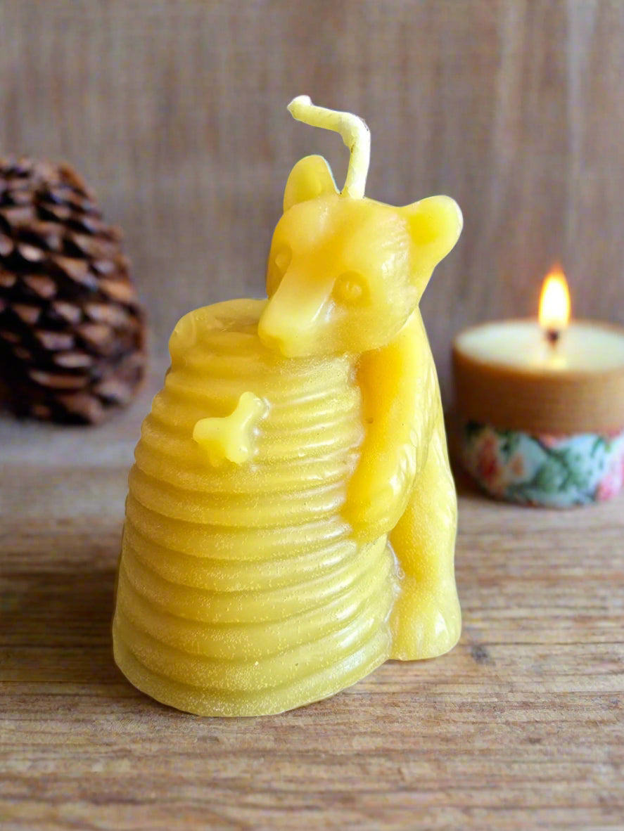 Yellow bear candle inside a beehive on a wooden surface with a lit candle in the background.